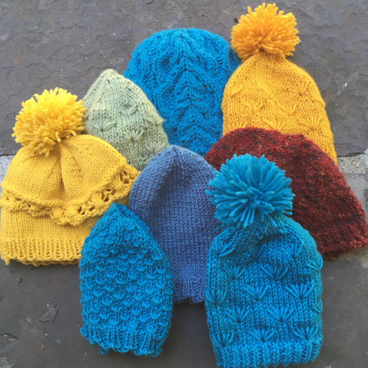 8 knit beanies in yellows, reds, blues, and greens against a stone background.