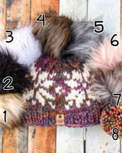 Load image into Gallery viewer, Snowflake Beanie in brown showing all pom options: cream, black, white, brown, gray/black, pink, gray, matching yarn. It is shown in a flat lay against a wooden background.
