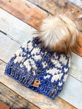 Load image into Gallery viewer, Snowflake Beanie in light blue with white snowflake and cream pom.  Shown here in a flat lay against a wooden background.
