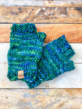 Load image into Gallery viewer, T Rex Mitts in green/blue in a flat lay against a wooden background.
