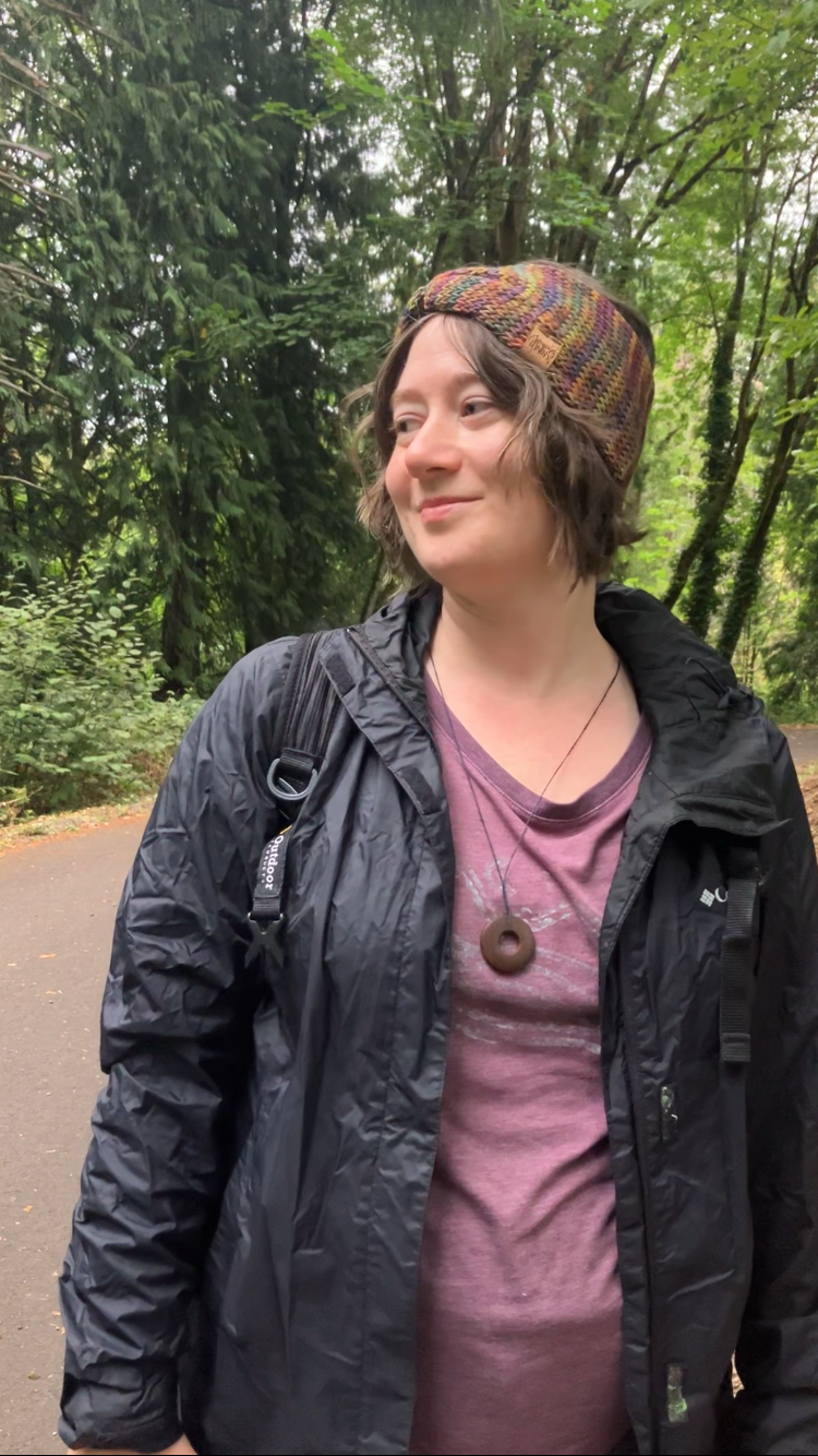 Knitted headband with knotted front shown on a model on a trail. The headband is a blend of rainbow colors, mostly yellow.