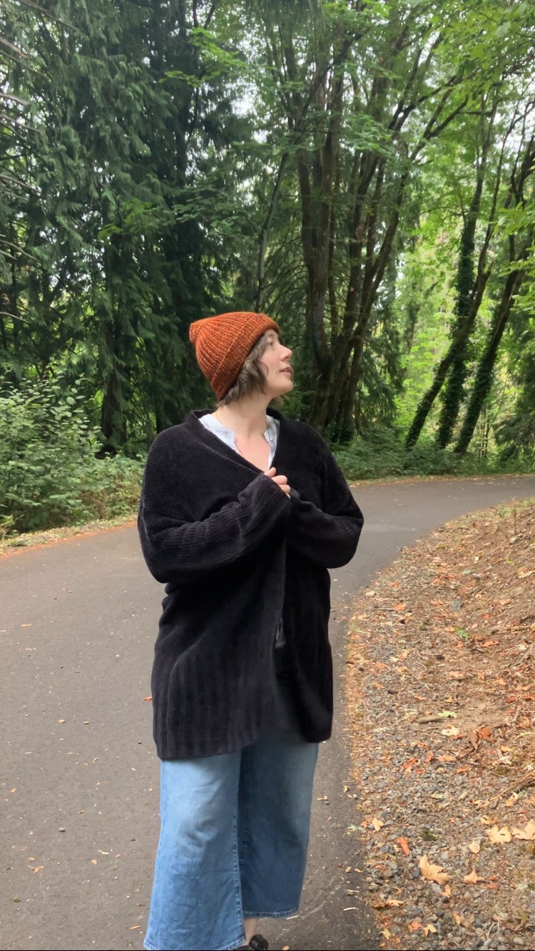 The Hadrosaur Hat is a lightweight, double layered slouchy beanie with folded brim. It is shown here in reddish orange on a model on a hiking trail.