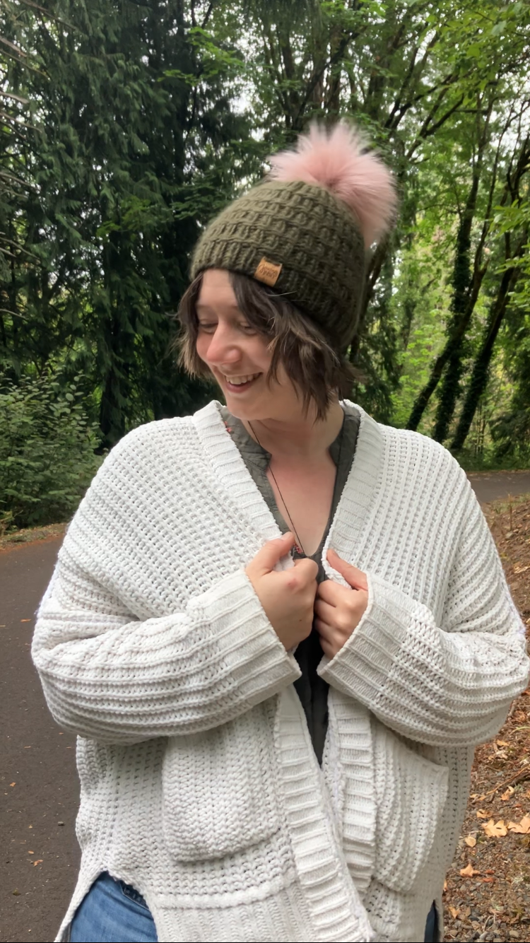 The Messenger Beanie in olive with pink pom shown on a model on a hiking trail.
