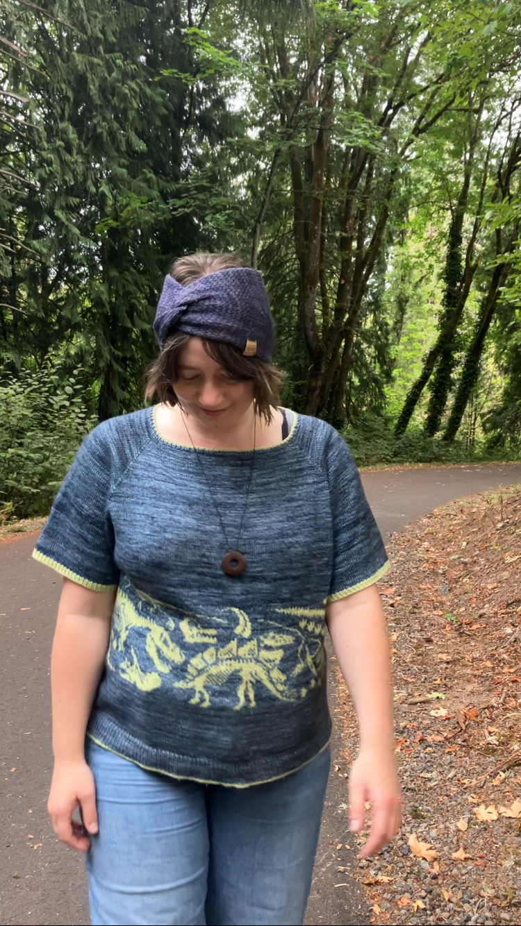 Knitted headband with knotted front shown on a model on a walking trail. The headband is a dark blue.