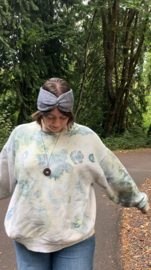 Knitted headband with knotted front shown on a model on a walking trail. The headband is light gray.
