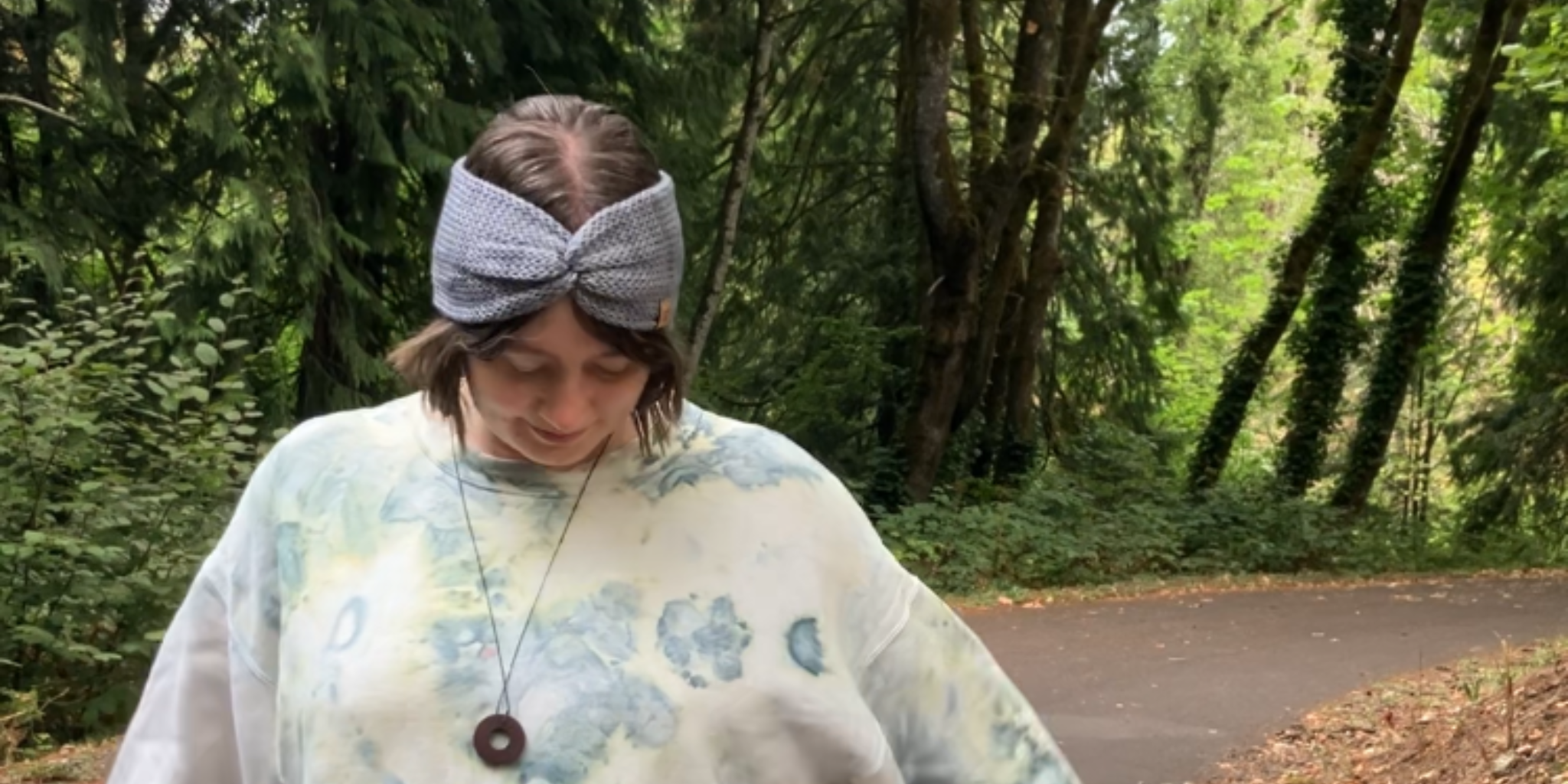 Knitted headband with knotted front shown on a model on a walking trail. The headband is light gray.
