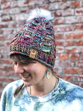 Load image into Gallery viewer, Fossil Beanie in rainbow with white pom.  It is shown here on a model.
