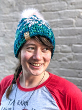Load image into Gallery viewer, Snowflake Beanie in teal with white snowflake and white pom.  It is shown here on a model.
