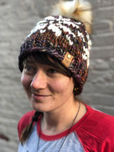 Load image into Gallery viewer, Snowflake Beanie in brown with white snowflake and cream pom.  It is shown here on a model.
