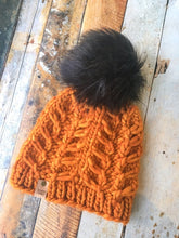Load image into Gallery viewer, Fossil Beanie in orange with black pom.  It is shown here in a flat lay against a wooden background.
