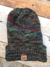 Load image into Gallery viewer, The Hadrosaur Hat is a lightweight, double layered slouchy beanie with folded brim.  It is shown here in dark rainbow (pocion) in a flat lay.
