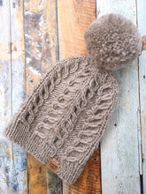 Load image into Gallery viewer, Fossil Beanie in beige with matching yarn pom.  It is shown here in a flat lay.
