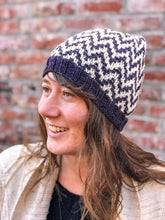 Load image into Gallery viewer, The Find Your Way Beanie has a chevron stripe pattern in two colors.  It is shown here on a model in white and navy.
