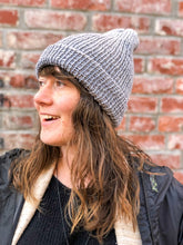 Load image into Gallery viewer, The Hadrosaur Hat is a lightweight, double layered slouchy beanie with folded brim. It is shown here in gray on a model.
