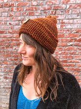 Load image into Gallery viewer, The Hadrosaur Hat is a lightweight, double layered slouchy beanie with folded brim. It is shown here in orange/brown on a model.
