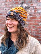 Load image into Gallery viewer, Lotus Beanie in gray with orange flowers and white/black pom. It is shown here on a model.
