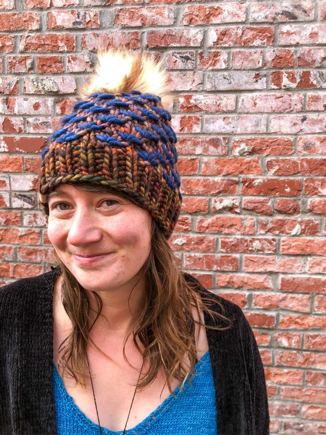 Lotus Beanie in brown with blue flowers and white/brown pom.  It is shown here on a model.