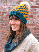 Load image into Gallery viewer, Lotus Beanie in teal with orange flowers and gray pom.  It is shown here on a model.
