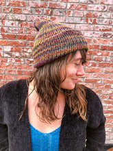 Load image into Gallery viewer, The Hadrosaur Hat is a lightweight, double layered slouchy beanie with folded brim. It is shown here in light rainbow (arco iris) on a model.
