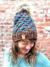 Load image into Gallery viewer, Lotus Beanie in brown with teal flowers and gray pom.  It is shown here on a model.
