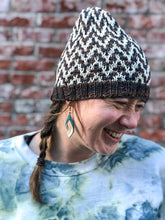 Load image into Gallery viewer, The Find Your Way Beanie has a chevron stripe pattern in two colors.  It is shown here on a model in white and blue/brown.

