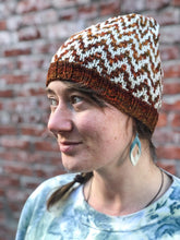 Load image into Gallery viewer, The Find Your Way Beanie has a chevron stripe pattern in two colors.  It is shown here on a model in white and orange.
