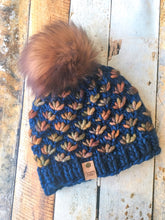 Load image into Gallery viewer, Lotus Beanie in blue with brown flowers and brown pom.  It is shown here in a flat lay.
