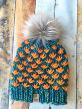 Load image into Gallery viewer, Lotus Beanie in teal with orange flowers and gray pom.  It is shown here in a flat lay.
