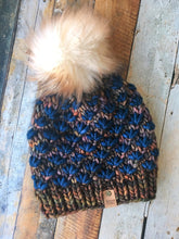 Load image into Gallery viewer, Lotus Beanie in brown with blue flowers and white pom.  It is shown here in a flat lay.
