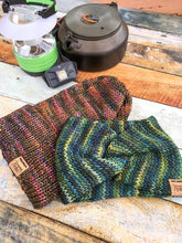 Load image into Gallery viewer, A folded brim slouchy beanie in flat lay with a knotted head wrap.  The hat has pink and green tones.  The wrap has yellow and blue tones.  In the background are camping supplies:  a kettle, a lantern, and a headlamp.
