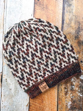 Load image into Gallery viewer, The Find Your Way Beanie has a chevron stripe pattern in two colors.  It is shown here in a flat lay in white and dark rainbow.
