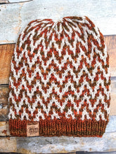 Load image into Gallery viewer, The Find Your Way Beanie has a chevron stripe pattern in two colors.  It is shown here in a flat lay in white and orange.

