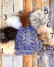 Load image into Gallery viewer, Fossil Beanie in light blue showing all pom options:  cream, black, white, brown, gray/black, pink, gray, matching yarn.  It is shown in a flat lay against a wooden background.
