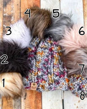Load image into Gallery viewer, Witch Hazel Beanie in gray showing all pom options: cream, black, white, brown, gray/black, pink, gray, matching yarn. It is shown in a flat lay against a wooden background.
