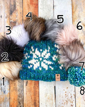 Load image into Gallery viewer, Snowflake Beanie in teal showing all pom options: cream, black, white, brown, gray/black, pink, gray, matching yarn. It is shown in a flat lay against a wooden background.
