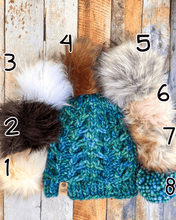 Load image into Gallery viewer, Fossil Beanie in blue/green showing all pom options:  cream, black, white, brown, gray/black, pink, gray, matching yarn.  It is shown in a flat lay against a wooden background.
