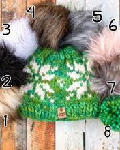 Load image into Gallery viewer, Snowflake Beanie in green showing all pom options: cream, black, white, brown, gray/black, pink, gray, matching yarn. It is shown in a flat lay against a wooden background.
