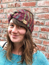 Load image into Gallery viewer, Knitted headband with knotted front shown on a model against a brick background.  The headband in a blend of bright rainbow colors, mostly pink.
