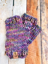 Load image into Gallery viewer, T Rex Mitts in rainbow (mostly purple) in a flat lay against a wooden background.

