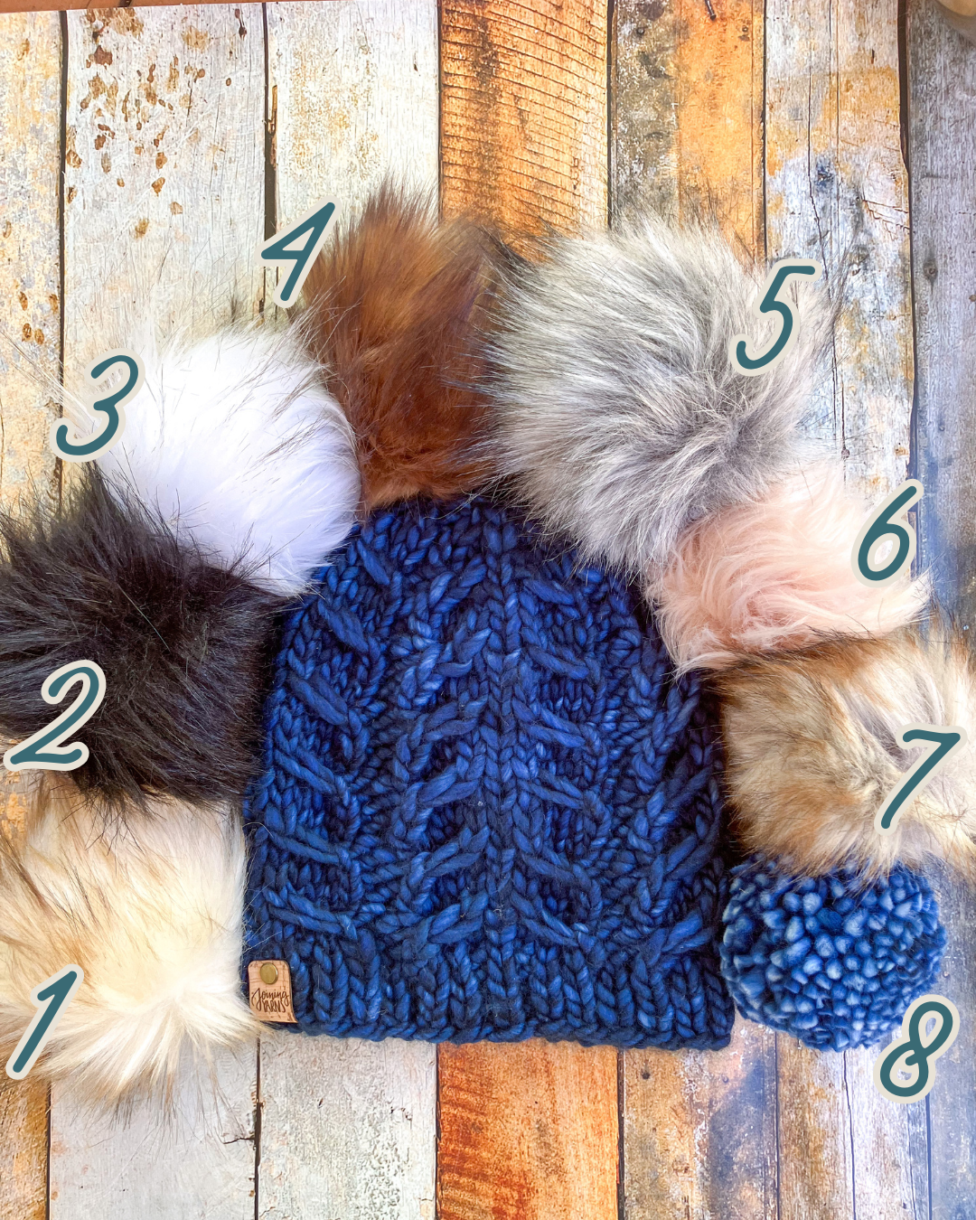 Fossil Beanie in dark blue shown in a flat lay with all 8 pom options.