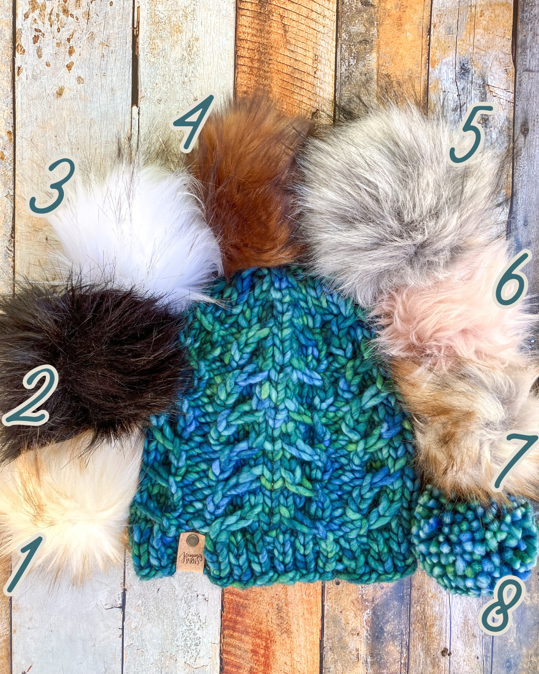 Fossil Beanie in teal shown in a flat lay with all 8 pom options.