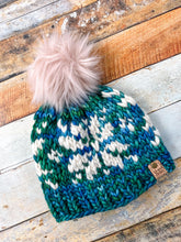 Load image into Gallery viewer, Snowflake Beanie in teal with white snowflake and pink pom.  Shown here in a flat lay against a wooden background.
