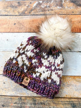 Load image into Gallery viewer, Snowflake Beanie in brown with white snowflake and cream pom.  Shown here in a flat lay against a wooden background.
