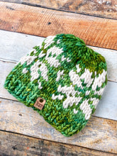 Load image into Gallery viewer, Snowflake Beanie in green with white snowflake and no pom.  Shown here in a flat lay against a wooden background.
