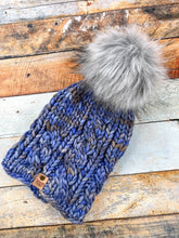 Load image into Gallery viewer, Witch Hazel Beanie in light blue with gray pom. It is shown here in a flat lay against a wooden background.
