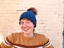 Load image into Gallery viewer, Witch Hazel Beanie in dark blue with brown pom. It is shown here on a model.
