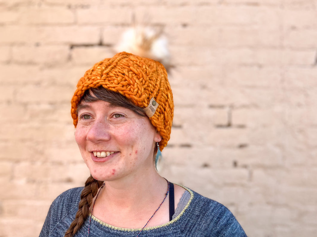 Witch Hazel Beanie in orange with cream pom. It is shown here on a model.