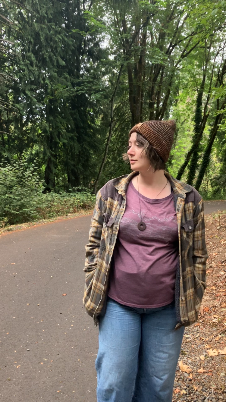 The Hadrosaur Hat is a lightweight, double layered slouchy beanie with folded brim. It is shown here in gold/purple/brown on a model on a hiking trail.