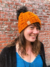 Load image into Gallery viewer, Fossil Beanie in orange with black pom.  It is shown here on a model.
