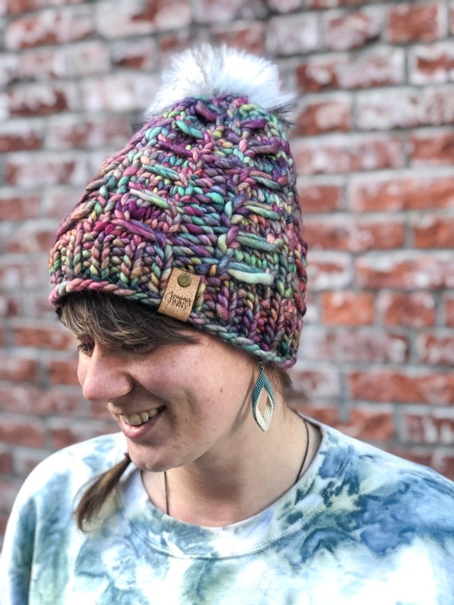 Fossil Beanie in rainbow with white pom.  It is shown here on a model.